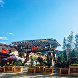 Illuminated building by trees against blue sky