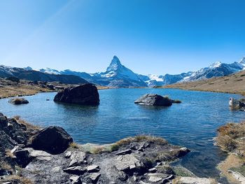 Scenic view of sea and mountains against clear blue sky