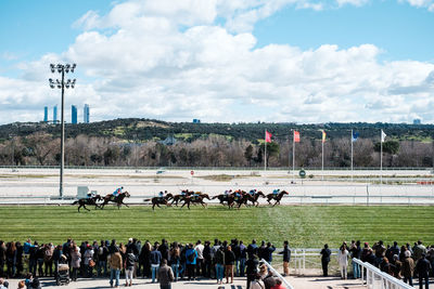 People watching horse race against cloudy sky
