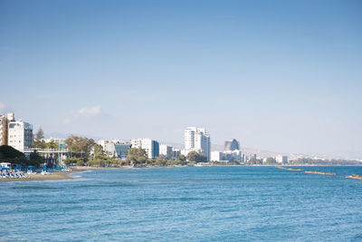 Sea by cityscape against blue sky