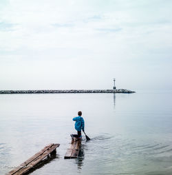 Rear view of man on pier over sea against sky