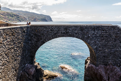 Distant view of people on arch bridge over sea