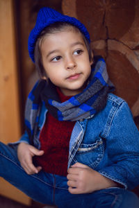Boy child in a blue denim jacket and hat is sitting at a wooden house