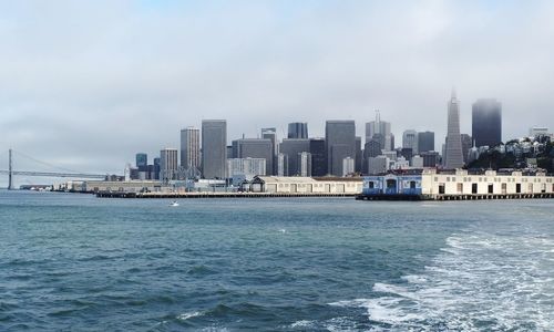 Sea by buildings in city against sky