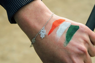 Close-up of tricolor paint on woman hand wearing bracelet outdoors