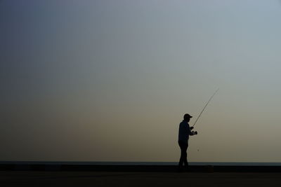 Silhouette man fishing against clear sky during sunset