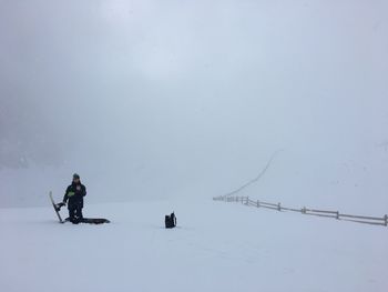 Man wearing warm clothing while kneeling on snow covered landscape during winter