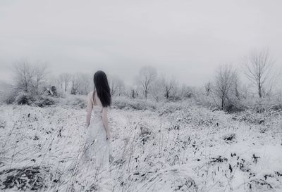 Woman standing on snow covered field against sky