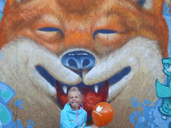 Portrait of girl sticking out tongue against mural wall