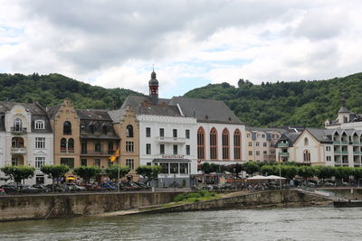 Buildings at waterfront against cloudy sky