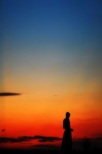 Silhouette man standing on beach against orange sky