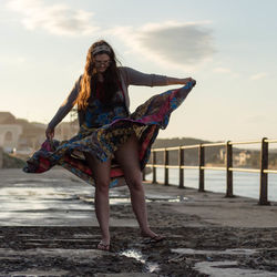 Portrait of young woman standing on beach against sky