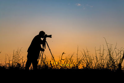 Silhouette of man photographing at sunset