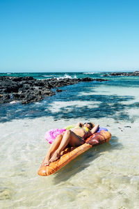 Rear view of woman relaxing at beach against clear sky