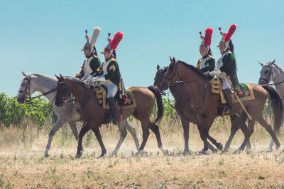 People riding horses on field against clear sky