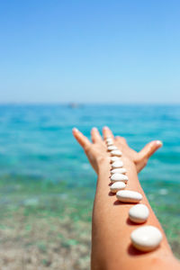 Cropped hand of woman sitting on beach against clear sky