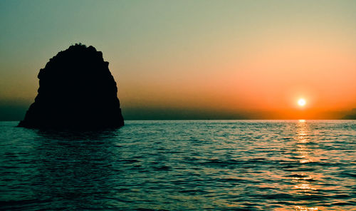 Silhouette rock in sea against sky during sunset