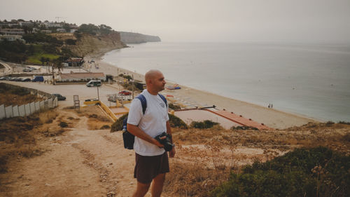 Mid adult man with camera against sea during sunset