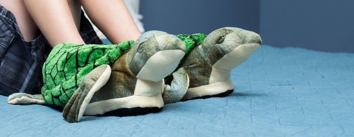 Low section of girl wearing turtle shaped shoes on bed at home