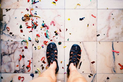 Low section of man standing by fallen confetti on tiled floor