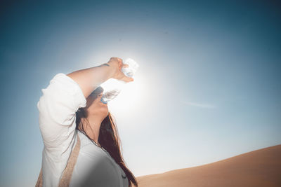 Low angle view of woman holding umbrella against blue sky