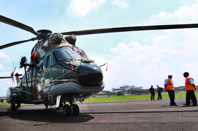 Men standing by helicopter on runway against sky