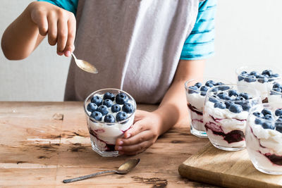 Boy holds homemade dessert with greek yogurt or cream, blueberry jam and fresh blueberries.