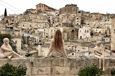 Rear view of woman sitting against buildings in city