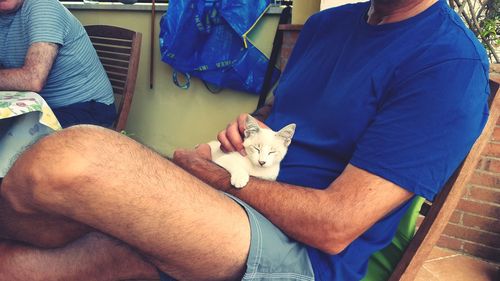 Midsection of man holding dog sitting at home