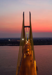 Illuminated bridge over sea against sky during sunset