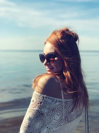 Young woman wearing sunglasses at beach against sky