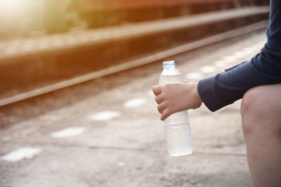 Midsection of person holding water bottle at railroad station