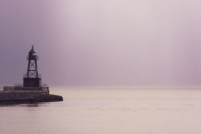 Lighthouse on beach by sea against sky