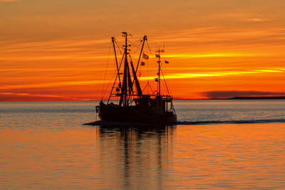 Silhouette boat in sea against orange sky