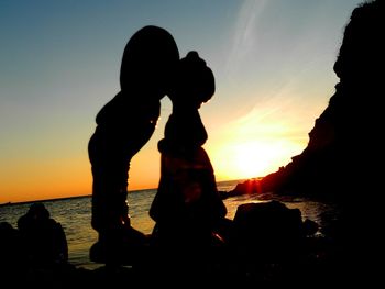 Silhouette people on rock at beach against sky during sunset