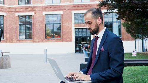 Businessman using laptop against building