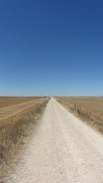 Road amidst field against clear blue sky