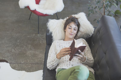 High angle view woman of with book relaxing on sofa at home