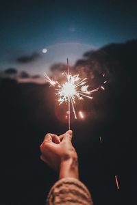 Low angle view of hand holding firework display at night