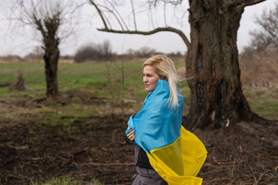 Smiling woman with ukrainian flag standing at field