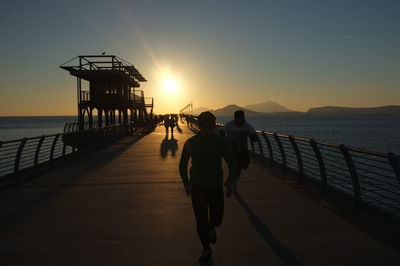 Silhouette of people standing on pier at sunset