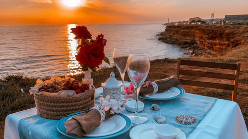 People on table by sea against sky during sunset