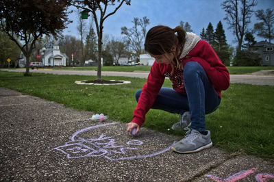 Full length of girl drawing on footpath in park