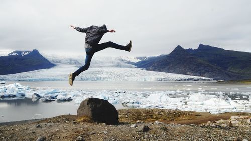 Man jumping on rock against sky