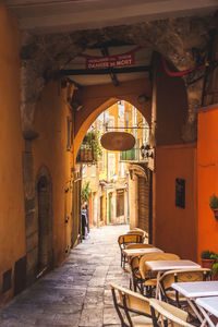 Tables and chairs in alley amidst buildings at sidewalk cafe