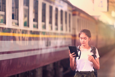 Young woman using mobile phone while standing at railroad station platform