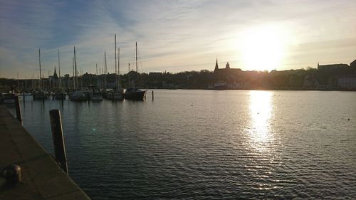 Sailboats moored on river by city against sky during sunset