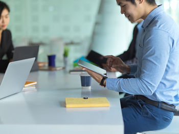 Side view of smiling businessman using digital tablet at office