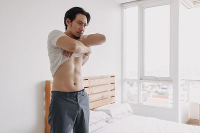 Young man looking away while standing on bed at home