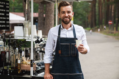 Portrait of barista holding coffee on street